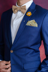 Man in blue suit with brown bow tie flower brooch and classic texture pocket square close up